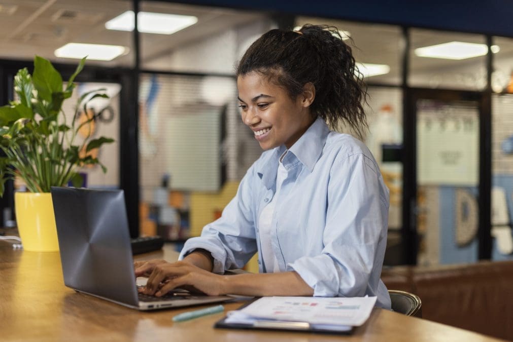 vista lateral de uma mulher sorridente trabalhando com um laptop no escritorio