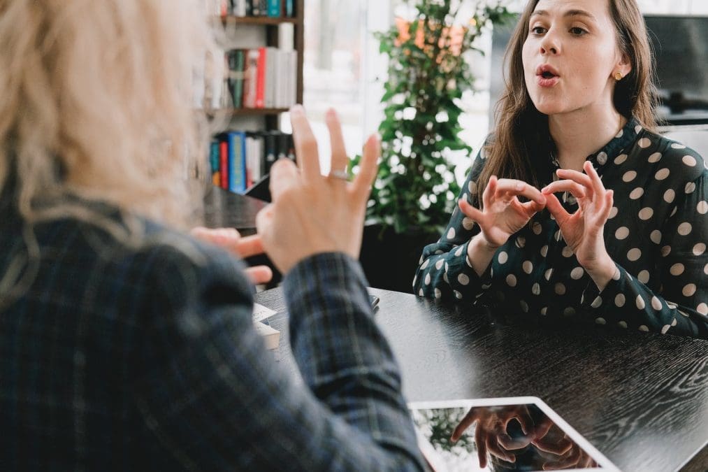 young female friends communicating using sign language in library
